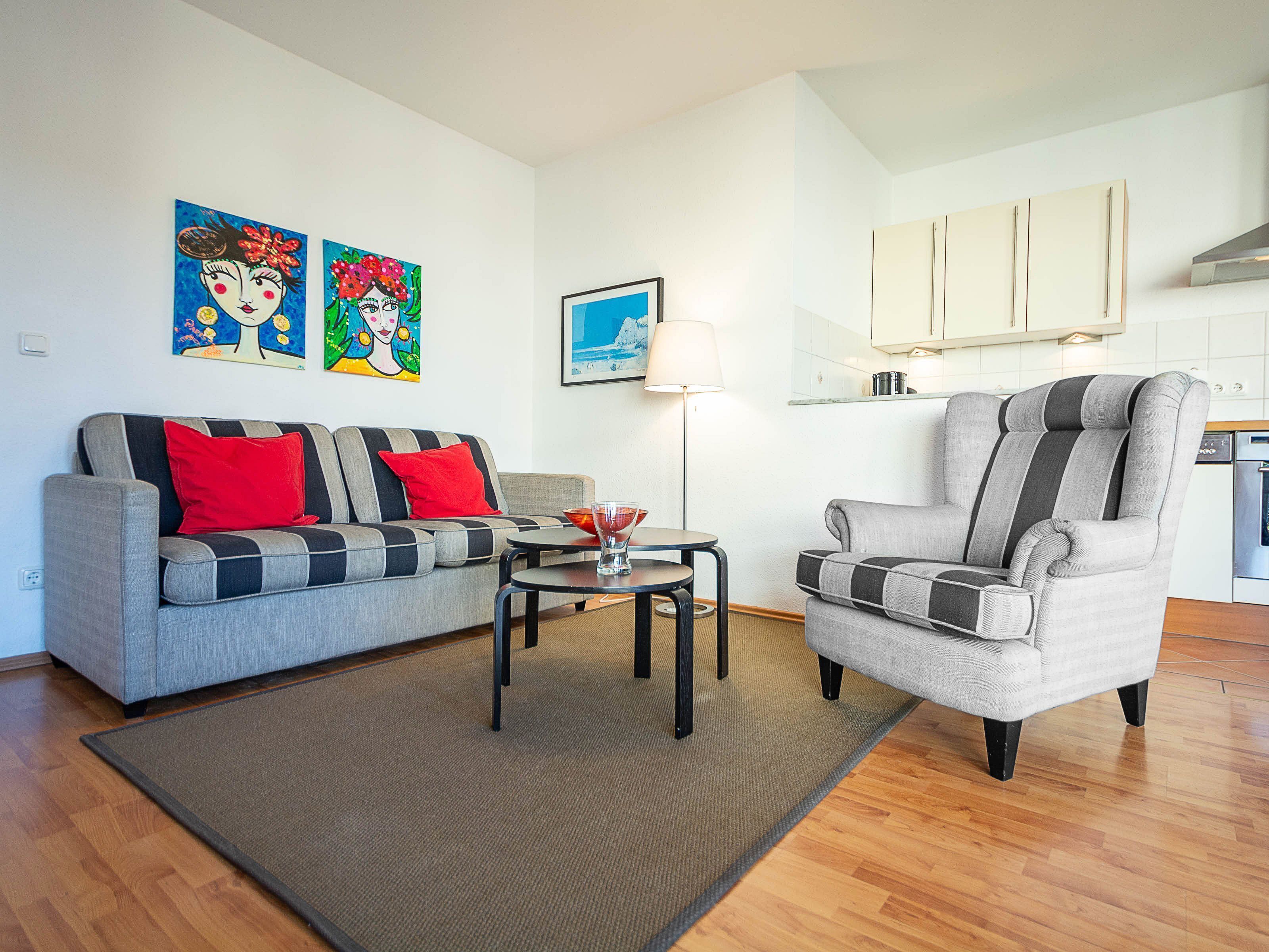 A living room with a sofa, armchair, coffee table, and artwork on the wall.