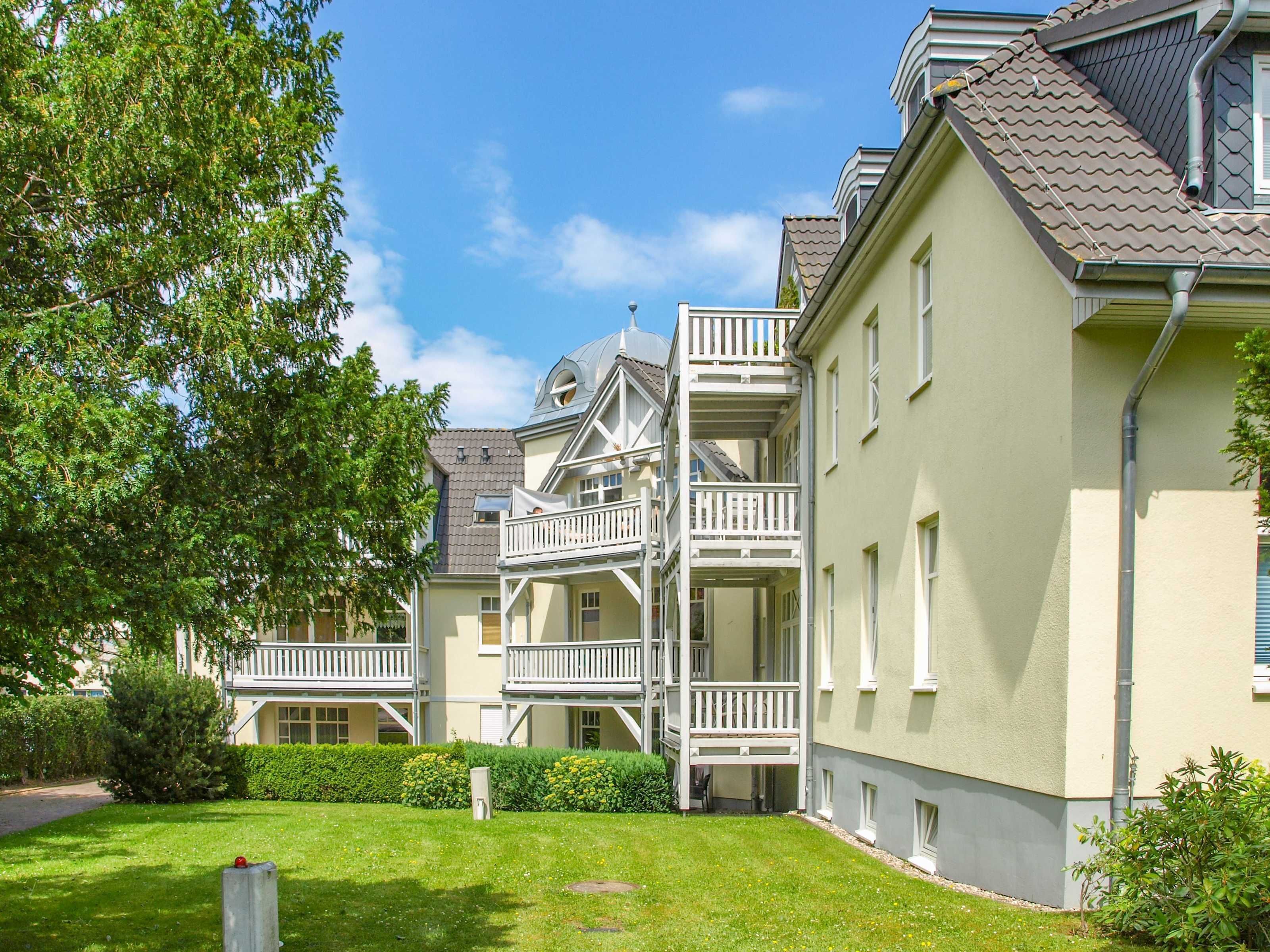 Ein mehrstöckiges Gebäude mit einem Balkon, einem gepflegten Rasen und blauem Himmel.