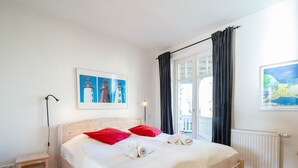 A neatly made bed with red pillows, a bedside table with a lamp, and a window with curtains. - Barbarossa Whg B-08. - B-08 (Kühlungsborn)