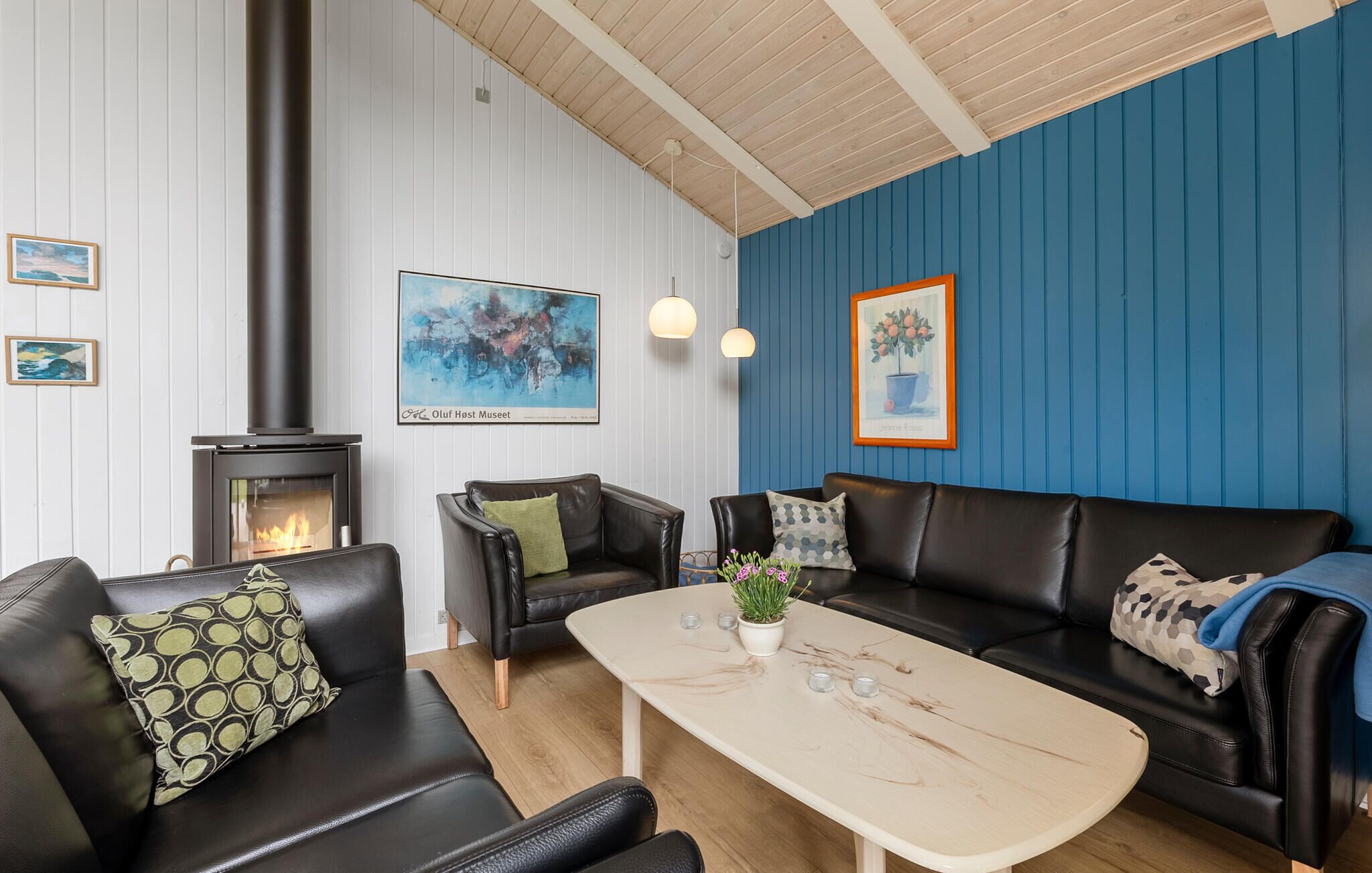 Ein modernes Wohnzimmer mit Kamin, schwarzen Ledersofas, einem Holztisch und blauen sowie weißen Wänden.