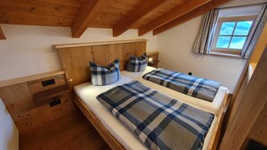 A bedroom with two beds, wooden headboard, checkered bedding, a window with curtains, and a wooden ceiling. - Double room Primerl - Anderlbauer am See (Schliersee)