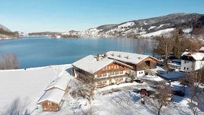 A large wooden building with a snow-covered roof, a ski lift, and a lake in the background. - Double room Primerl - Anderlbauer am See (Schliersee)