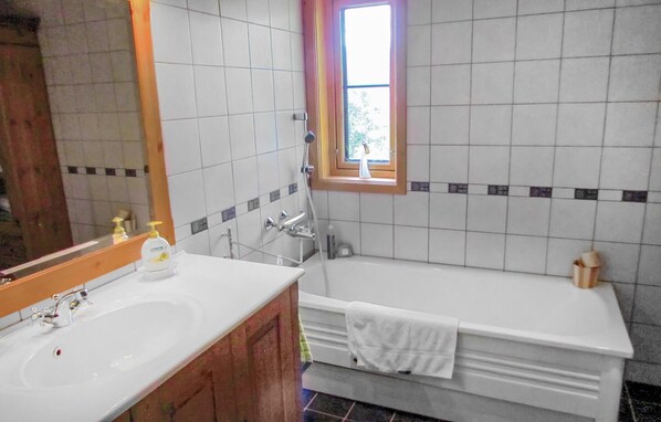 Ein Badezimmer mit einem weißen Waschbecken, einer Badewanne und einem Fenster mit Blick auf Grünflächen.