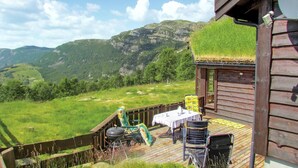 Une cabane en bois dotée d’une terrasse, de meubles de jardin et offrant une vue sur un paysage montagneux.
