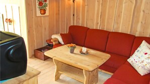 Une pièce chaleureuse avec un plancher en bois, un canapé rouge, une table basse en bois et un téléviseur posé sur un meuble.