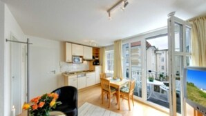 A modern apartment with a kitchen, dining area, and large windows offering a city view. - Villa Aquamarina Whg. 18, SOUTH FACING BALCONY, CHAIR - Villa Aquamarina, 1st ROW, partly. (Heringsdorf)