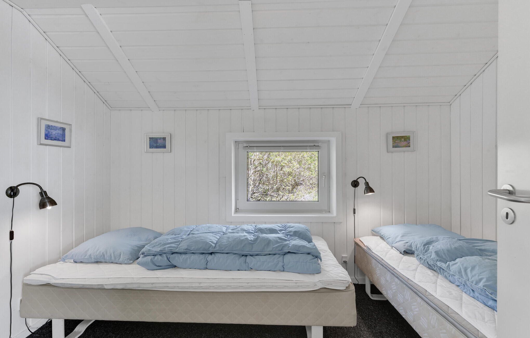 Une chambre avec deux lits, une fenêtre et deux lampes fixées au mur.