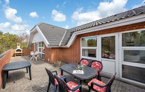 A patio with a brick wall, a grill, and a table with chairs.