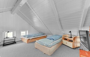 A compact, well-lit attic bedroom with two single beds, a desk, and a TV.