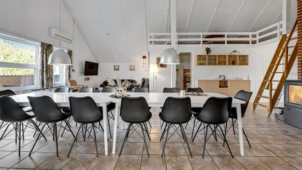 A spacious dining area with a long table and modern chairs, a loft with a wooden ladder, and a cozy seating area with a fireplace. - Lovely home in Ringkøbing with sauna (Ringkøbing)