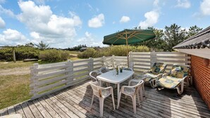 A wooden deck with a table and chairs, a green umbrella, and a brick wall. - Lovely home in Ringkøbing with sauna (Ringkøbing)
