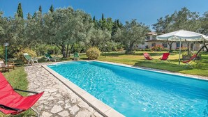 Una piscina con baldosas de piedra, rodeada de vegetación y un edificio de piedra.