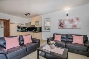 A modern living room with two leather sofas, a coffee table with a vase, and a kitchen in the background.