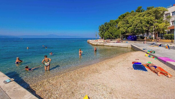 Una playa con aguas cristalinas, gente nadando y un hotel al fondo.