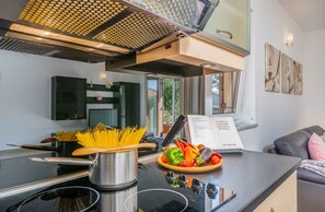 A modern kitchen with a stove, pots, and a variety of fresh vegetables on the counter.