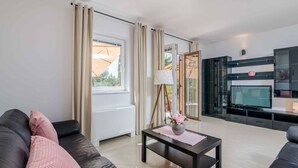 Una sala de estar moderna con un sofá, una mesa de centro con un florero, un televisor y un aparador de vidrio.