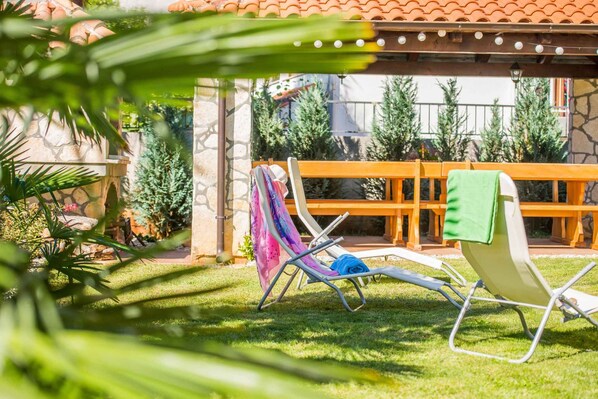 A patio with two lounge chairs, one with a towel and a colorful cloth, and a wooden bench in the background.