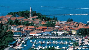 An aerial view of a coastal town with a marina, buildings with red-tiled roofs, and a prominent tower.