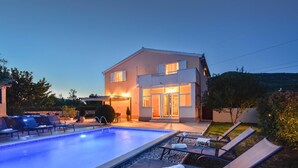 A modern two-story house with a swimming pool, outdoor seating, and a well-lit entrance.