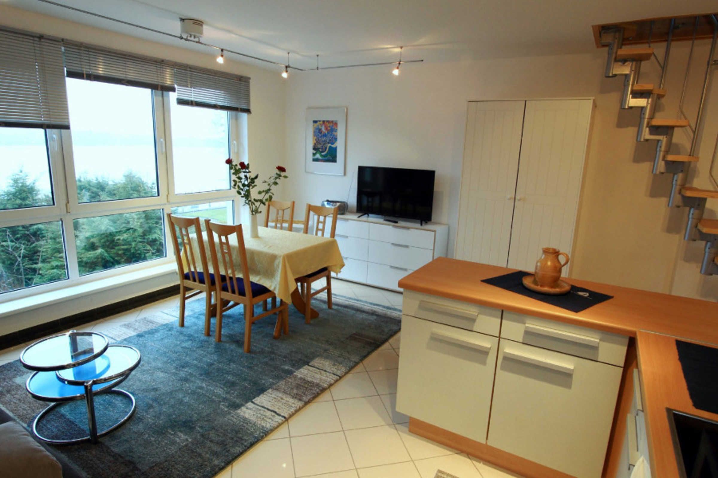 A modern kitchen with a dining area, large windows, and a TV.