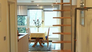 Un pasillo con una escalera de madera, un comedor con mesa y sillas, y una cocina con armarios y encimera.