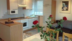 Una cocina moderna con armarios blancos, un microondas y un lavamanos. Hay dos rosas rojas sobre la mesa y una ventana con persianas.