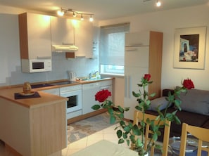 A modern kitchen with white cabinets, a microwave, and a sink. There are two red roses on the table and a window with blinds. - Vacation apartment at Lake Mirower See (attic) Whg. 1 - Holiday apartments at the lake in (Mirow)