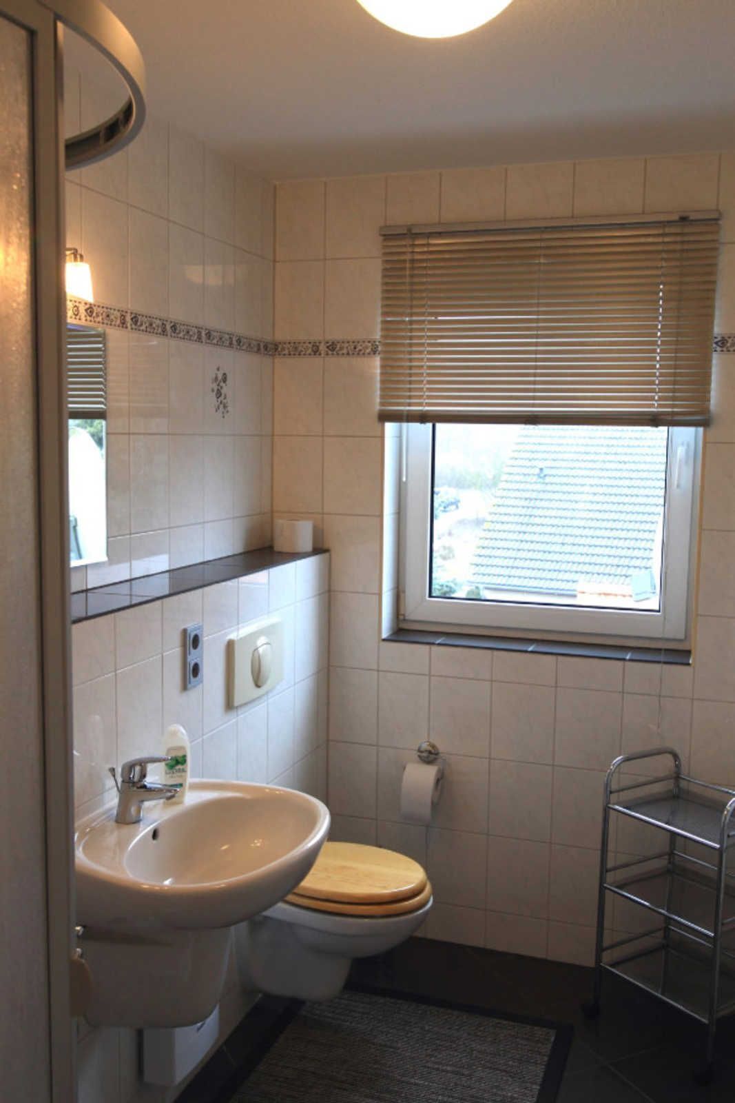 Ein kleines Badezimmer mit Waschbecken, Toilette und Fenster mit Jalousien.