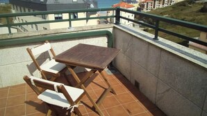 A balcony with a table and chairs, overlooking a coastal town and the sea.