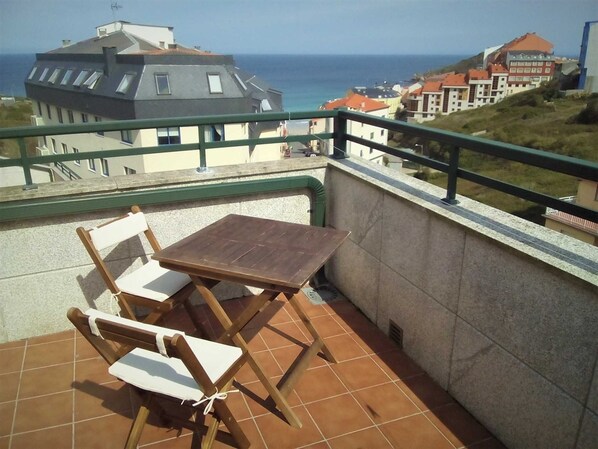 Un balcón con mesa y sillas, con vistas a un pueblo costero y al mar.