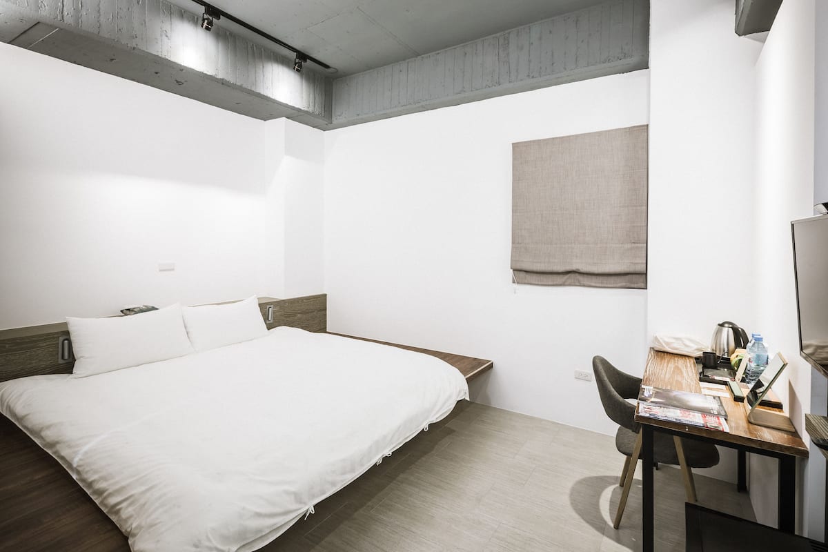 A hotel room with a large bed, a desk with a laptop, and a small table with a water bottle.