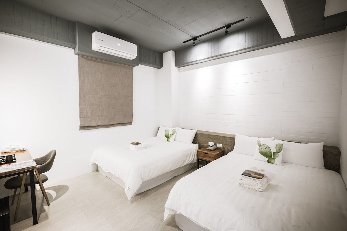 A hotel room with two beds, a desk, and a chair. There is an air conditioning unit on the wall.