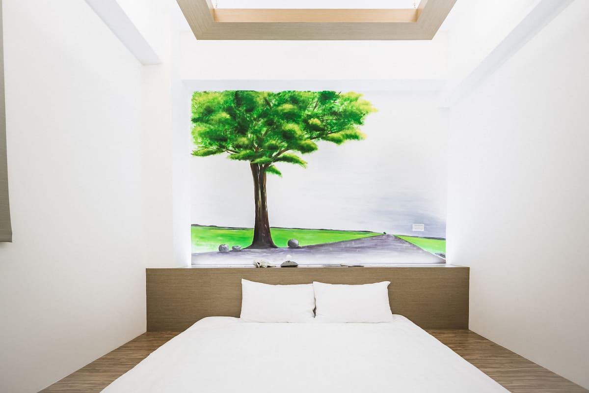 A bedroom with a large bed, a headboard, and a painting of a tree on the wall.