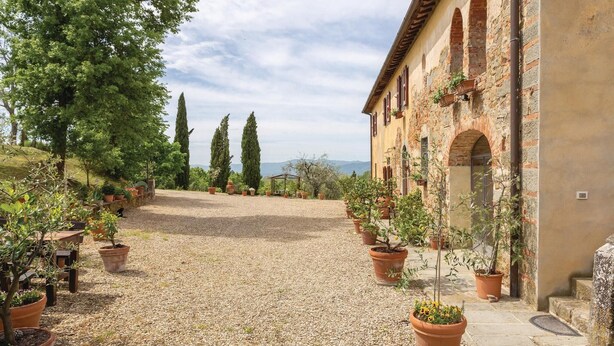 A courtyard with a gravel path, potted plants, and a building with arched windows and a tiled roof. - Beautiful home in Reggello FI (Reggello FI)