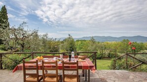 An outdoor dining area with a table set for two, surrounded by a rustic wooden fence, overlooking a lush garden and distant mountains. - Beautiful home in Reggello FI (Reggello FI)
