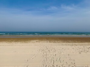 Une plage où l’on voit des empreintes de pas menant à l’eau, un ciel dégagé et une mer calme.