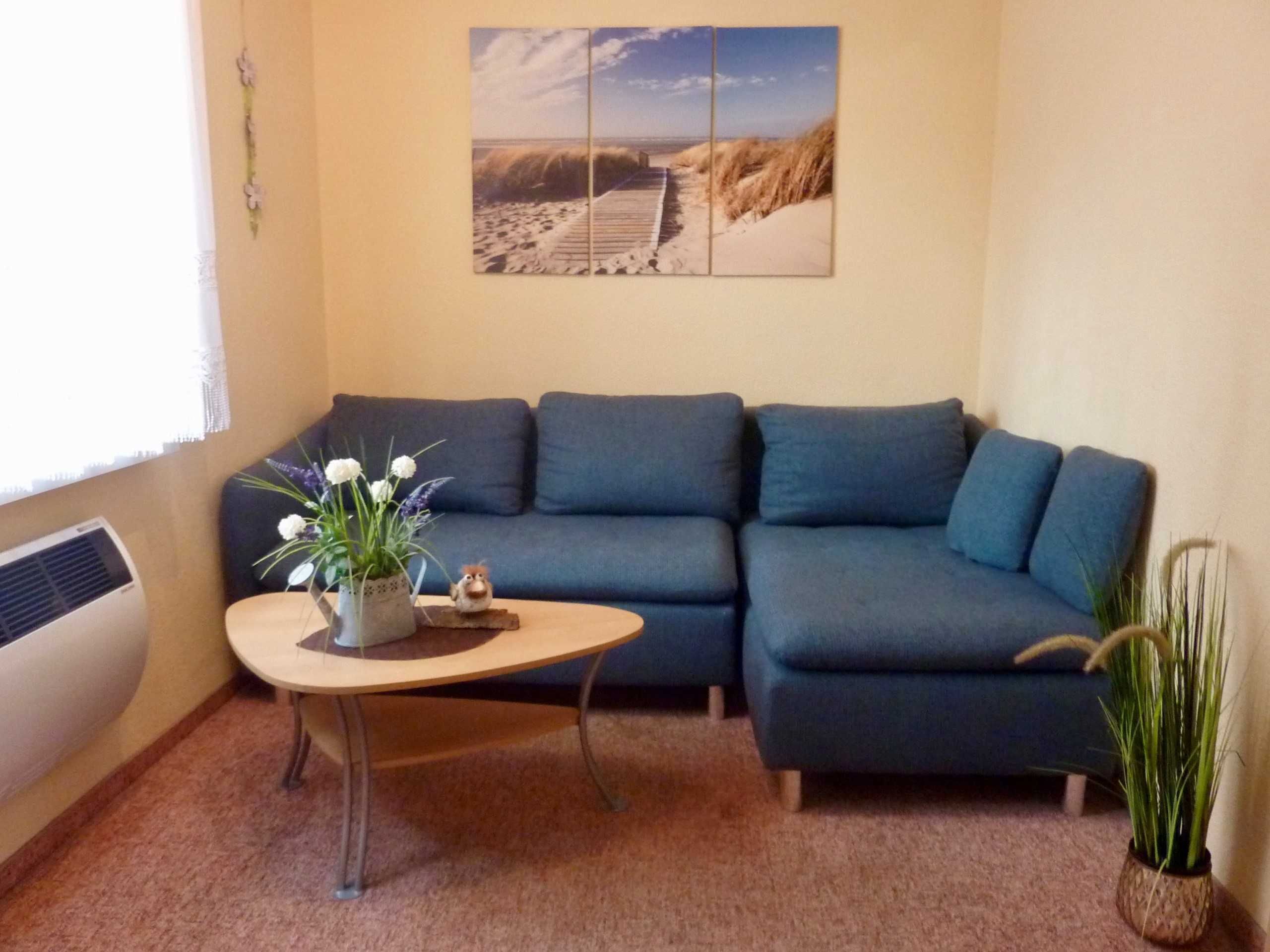 A living room with a blue sofa, a small coffee table with a plant, and a beach-themed wall art.