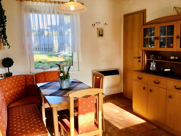 Un coin repas chaleureux avec une table dressée pour deux personnes, un buffet en bois aux portes vitrées et une fenêtre donnant sur l’extérieur.