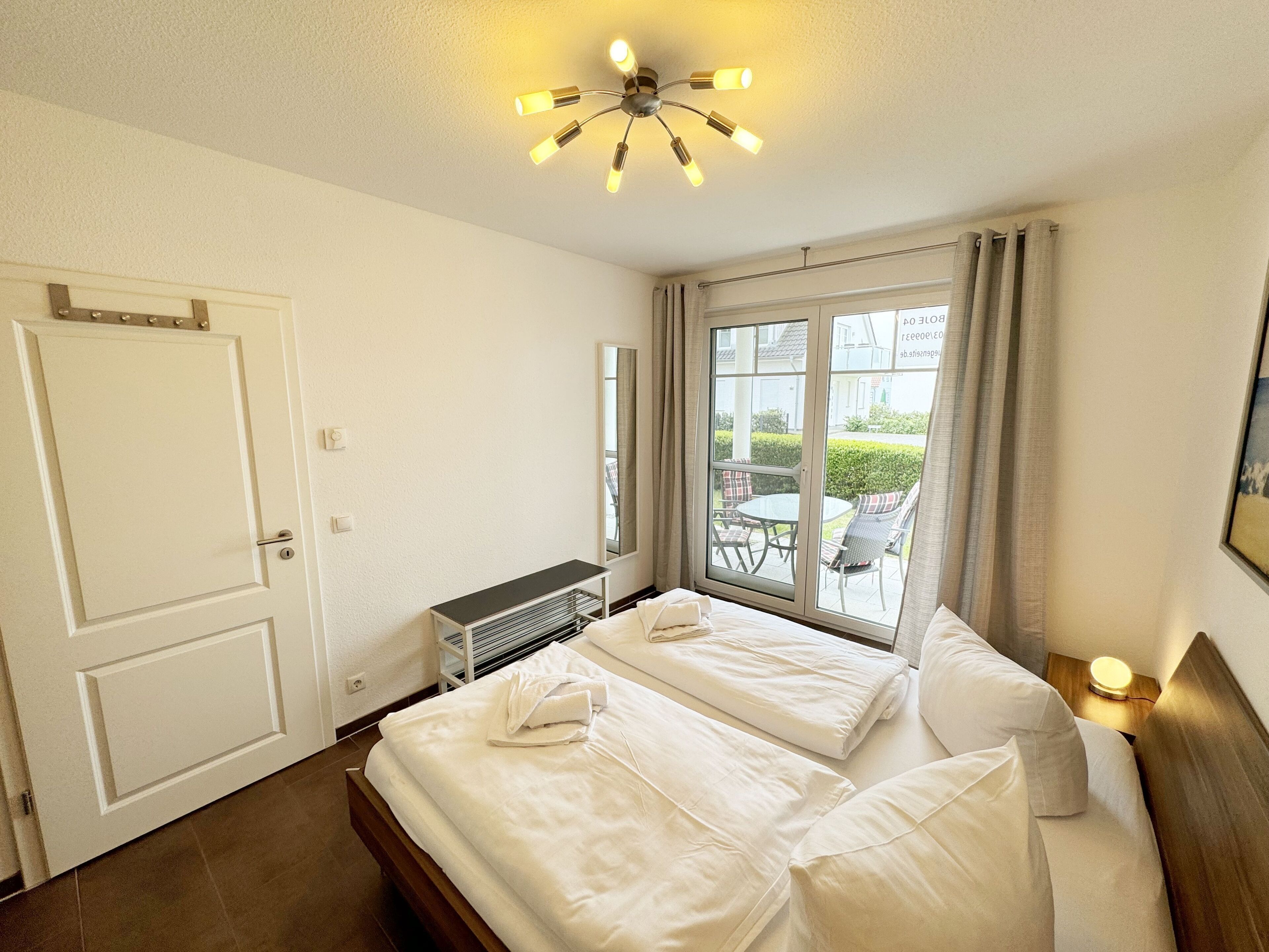 Habitación de hotel con cama, ventana con vistas al exterior, lámpara de techo y una puerta.