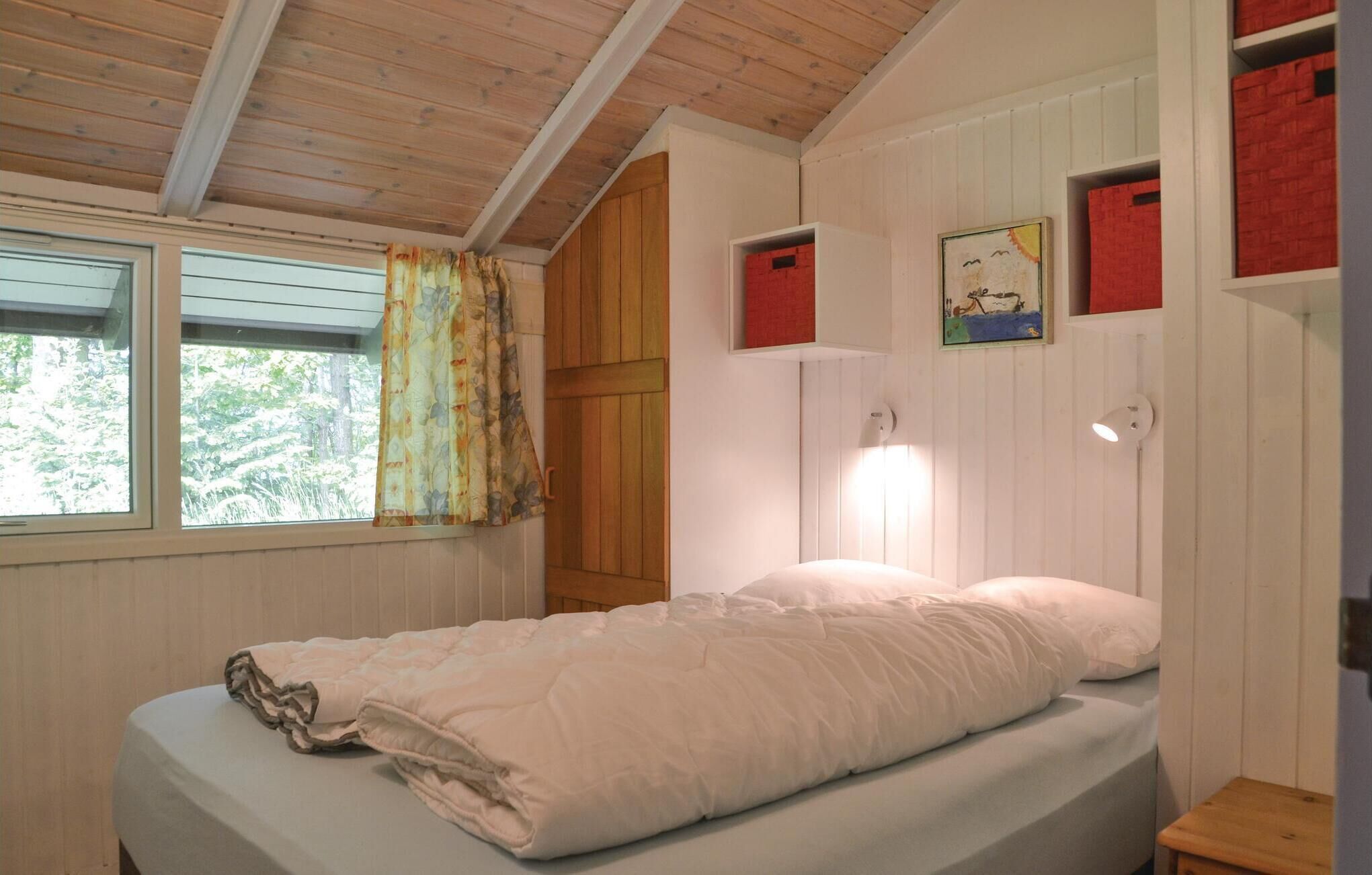 A bedroom with a bed, a window with curtains, a wall-mounted shelf with a picture, and a wooden ceiling.