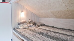 A cozy attic bedroom with a sloped ceiling, wooden walls, and a bed with patterned bedding. - Pet friendly home in Ansager with WiFi (Ansager)