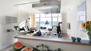 Una cucina moderna con un'ampia finestra vista mare, un'area pranzo con sedie nere e un bancone con un'anguria.