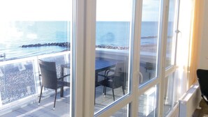 Un balcone con tavolo e sedie, affacciato su una costa rocciosa e il mare.