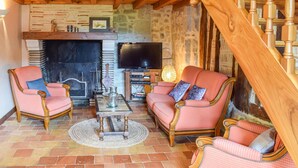Uma sala de estar aconchegante com lareira, duas poltronas, um sofá, uma televisão e uma escada de madeira.