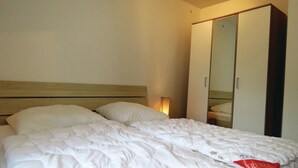 A bedroom with a bed, pillows, a wooden headboard, a wardrobe, and a bedside lamp. - Ferienhaus 7 in Thalfang (Thalfang)