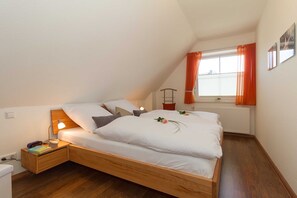 A bedroom with a wooden bed, bedside tables, a nightstand, a window with orange curtains, and a radiator. - Holiday house Möwengarten am Haff - holiday home Möwengarten am Haff (Rerik)