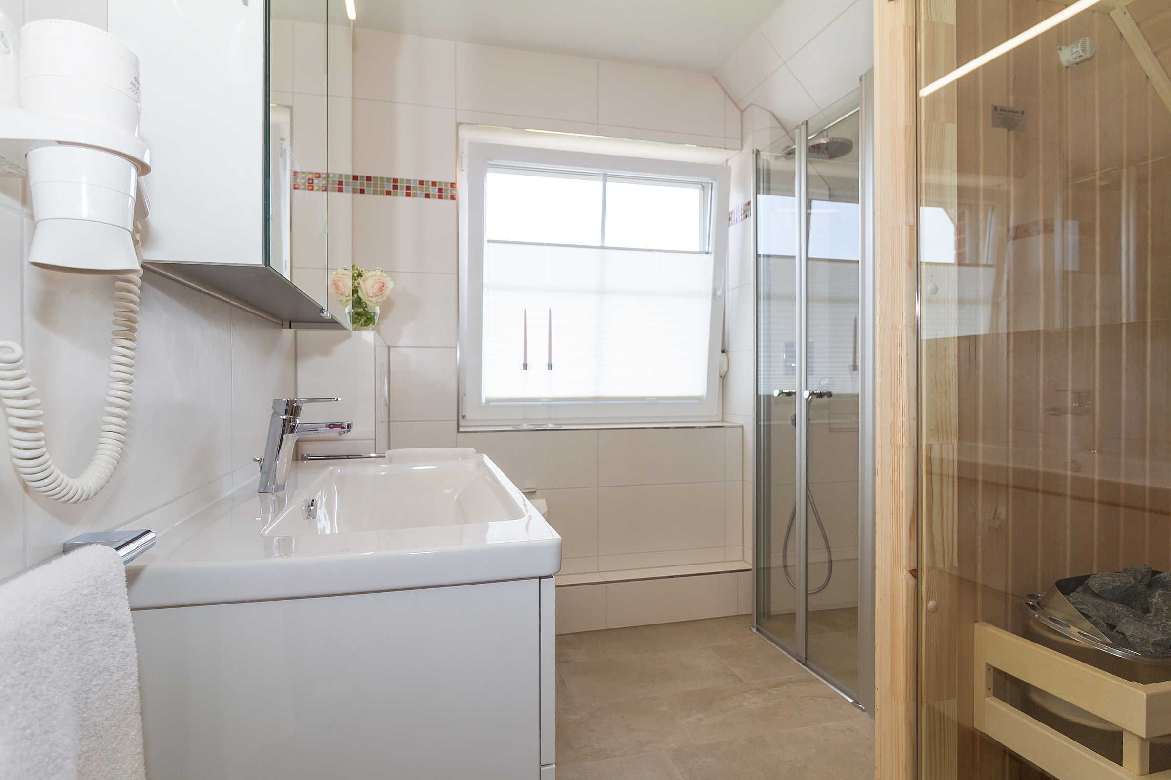 A bathroom with a sink, a hairdryer, a shower, and a window.