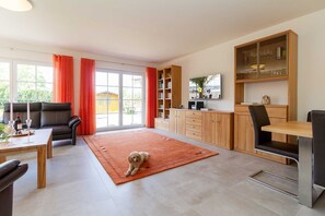 A modern living room with a sofa, a dining table, a rug, and a dog. - Holiday house Möwengarten am Haff - holiday home Möwengarten am Haff (Rerik)