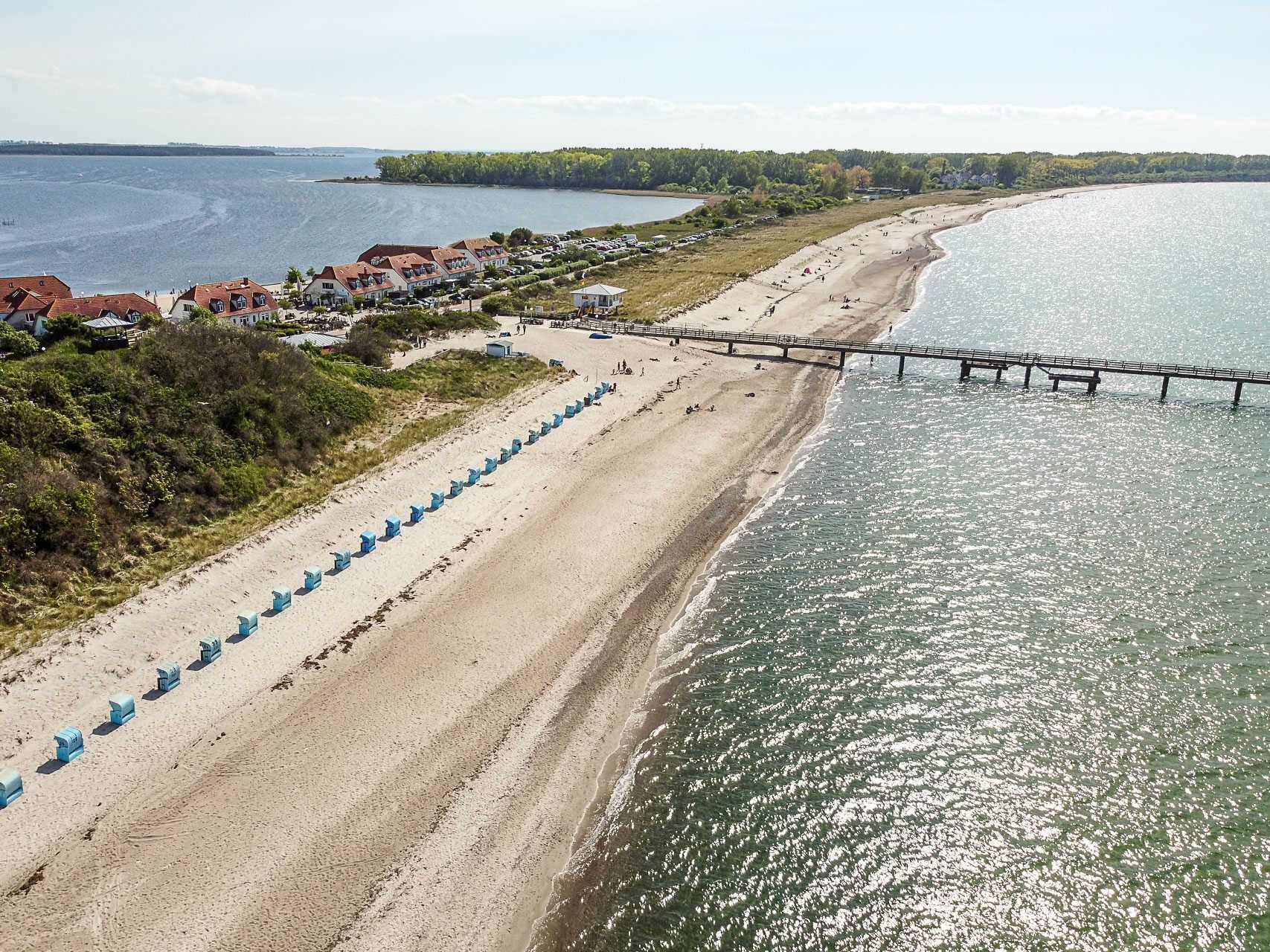 A beach with a pier, sandy shore, and a row of blue beach huts.