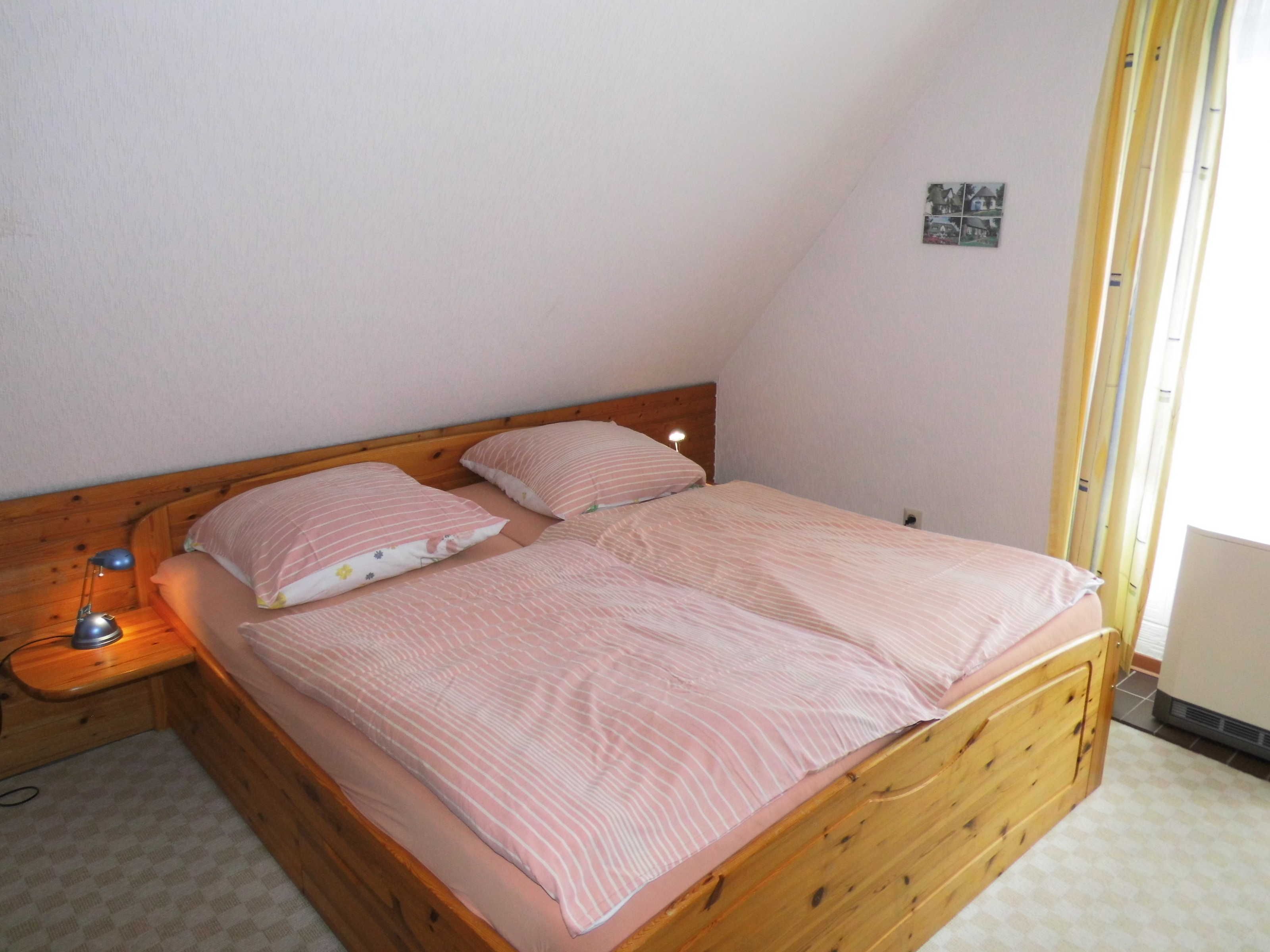 Un lit simple avec une tête de lit en bois, dans une pièce dont le plafond est en pente.